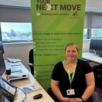 Colleague Helene Hainey with Your Next Move Working North Ayrshire roller banner behind her, sitting at office desk