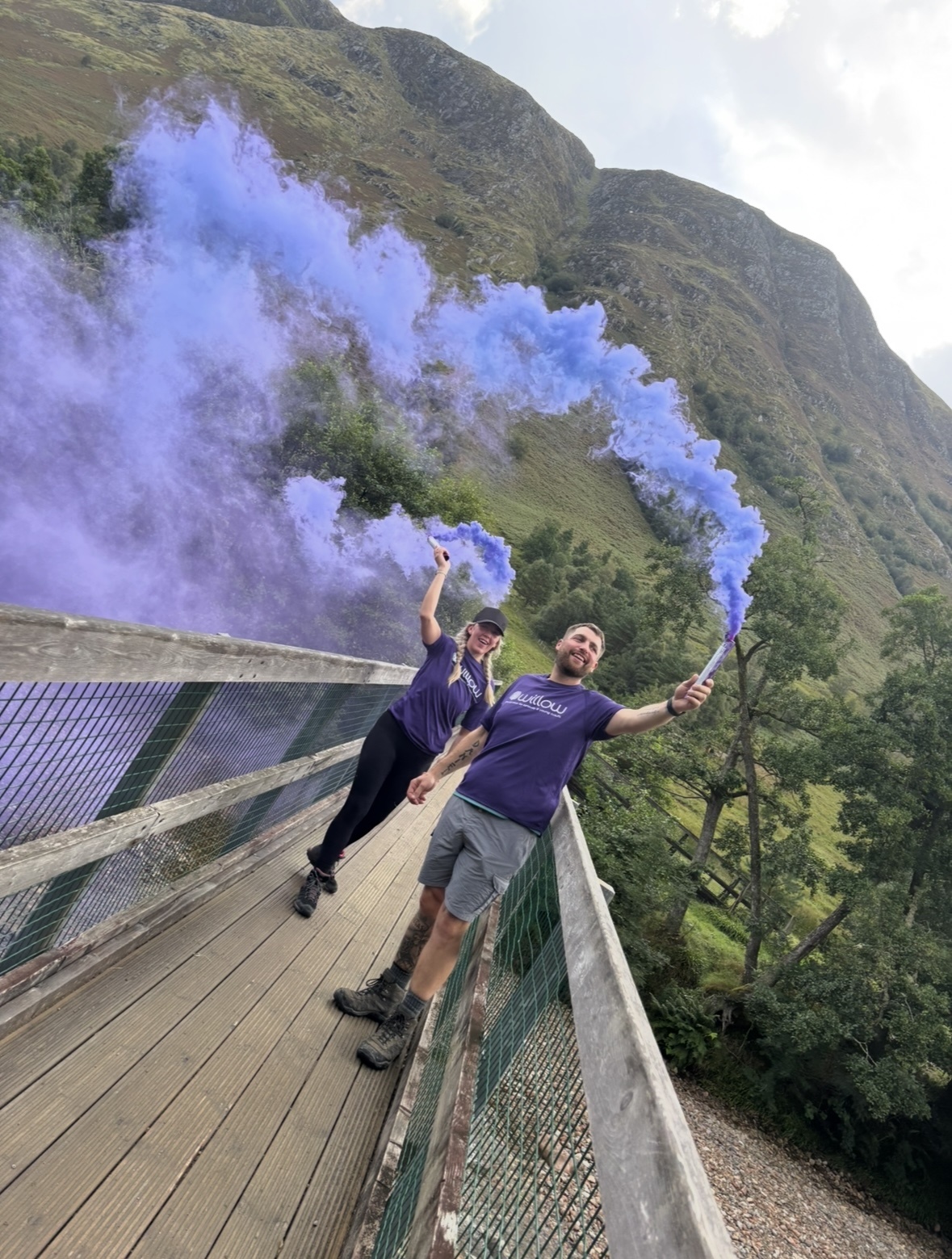 Colleague and partner holding purple flares at top of mountain during recent challenge