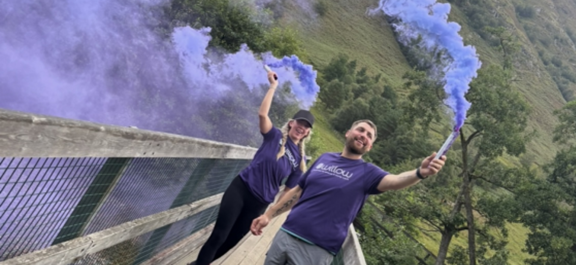 Colleague and partner holding purple flares at top of mountain during recent challenge