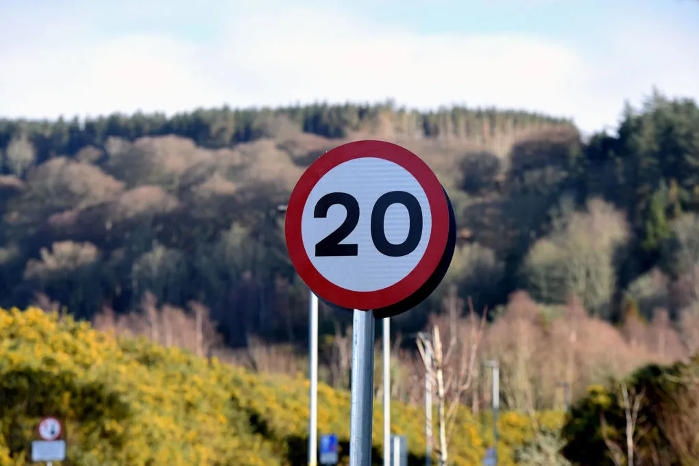 A 20mph road sign on a sunny day with hills and trees in the background