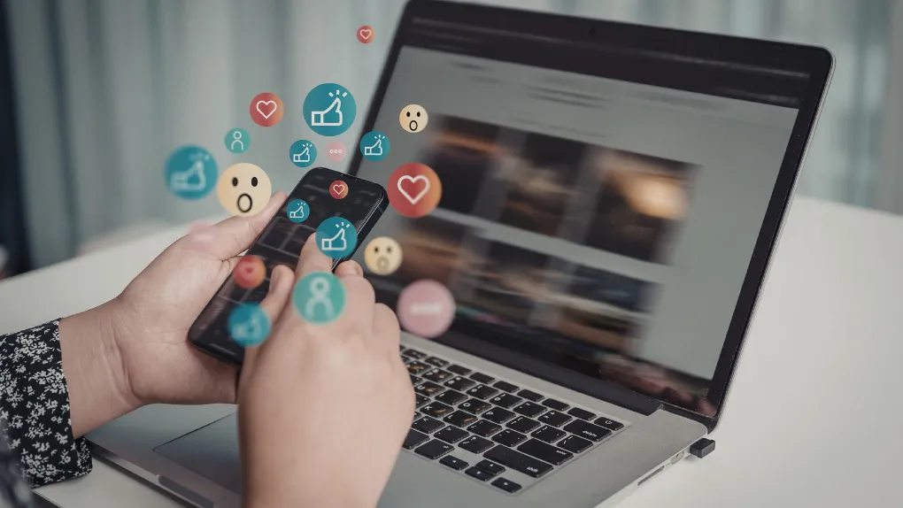 Laptop with person using phone and emoji social media icons