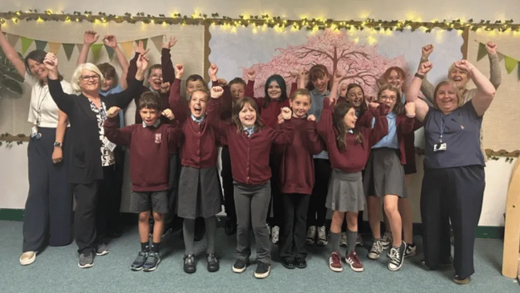 Children and staff at a school throwing their arms up in celebration